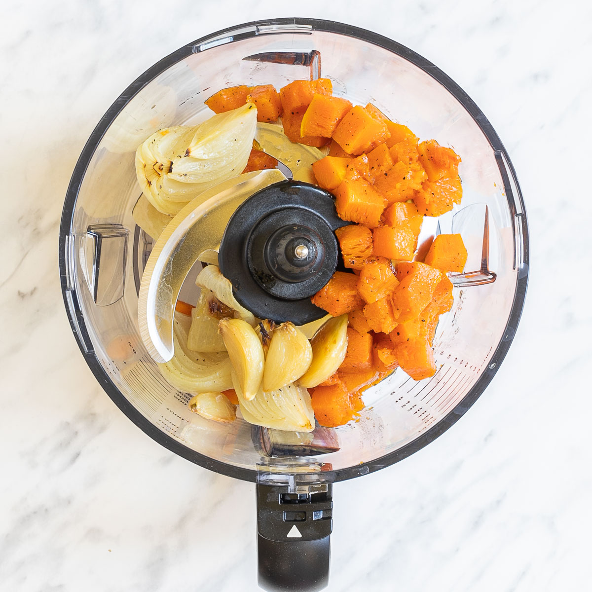 Food processor with orange squash cubes, garlic and onion wedges.