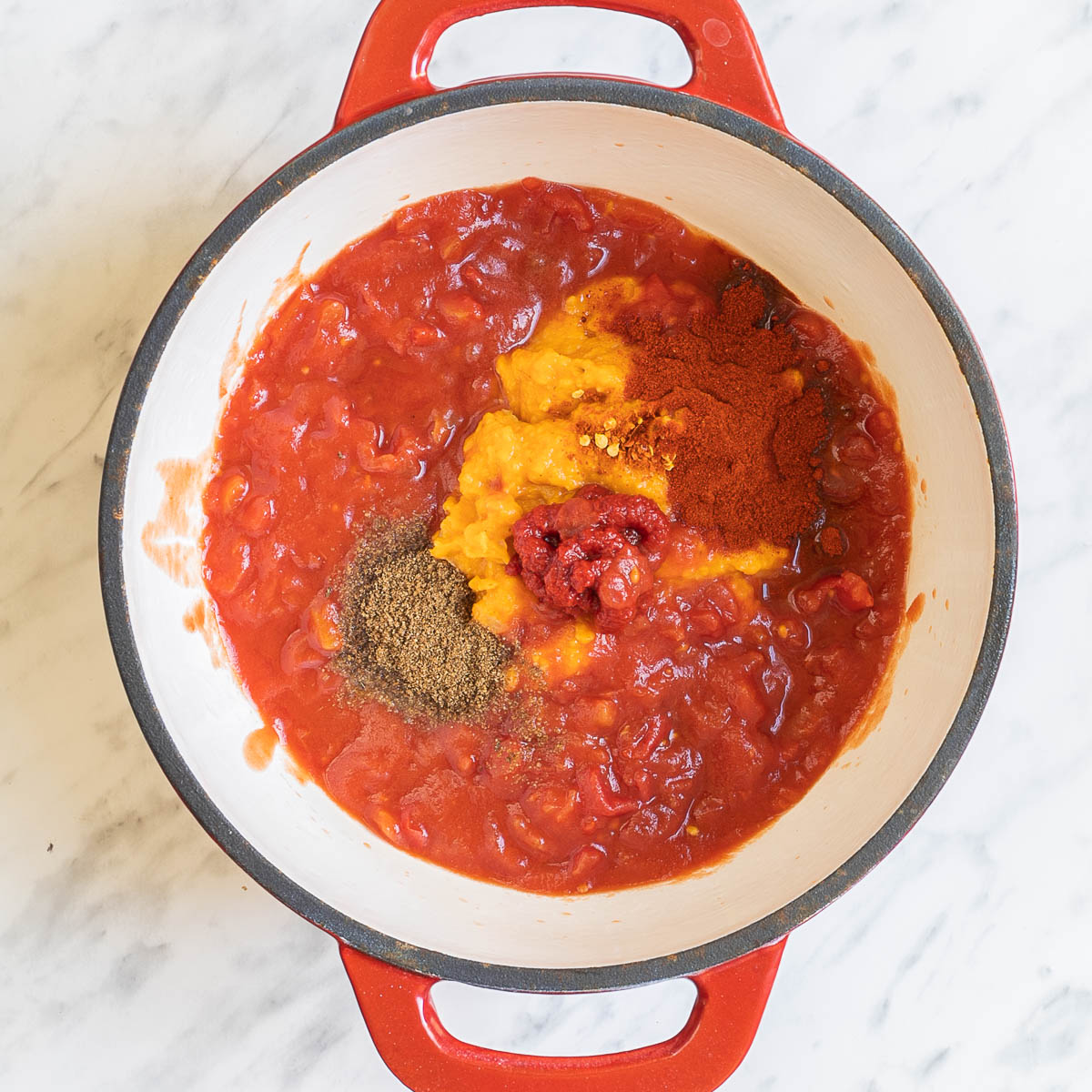 White-red enameled Dutch oven with red sauce and heaps of orange puree and spices.