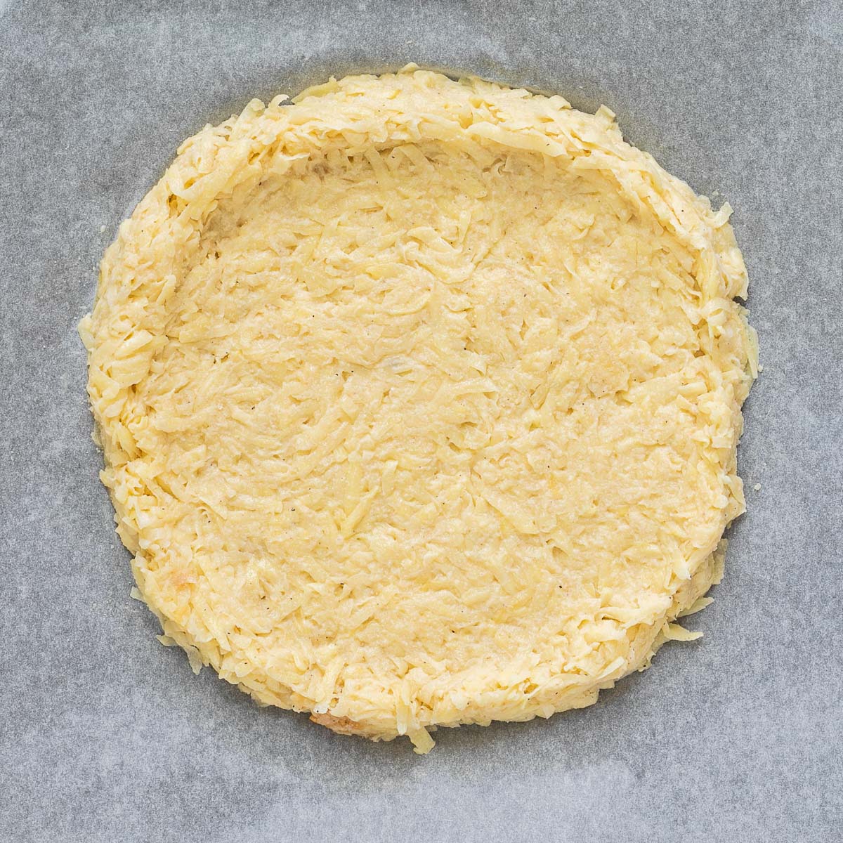 Shredded potato pizza crust on a pachment paper.