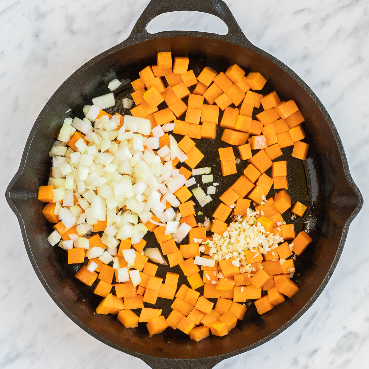 Cast iron with orange squash cubes and heaps of minced onion and garlic.