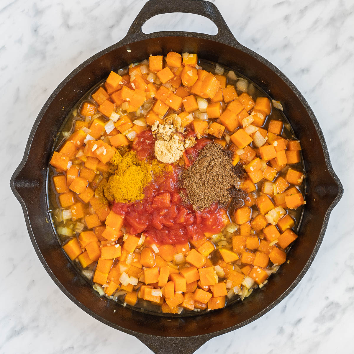 Cast iron skillet with orange squash cubes and small heaps of different spices