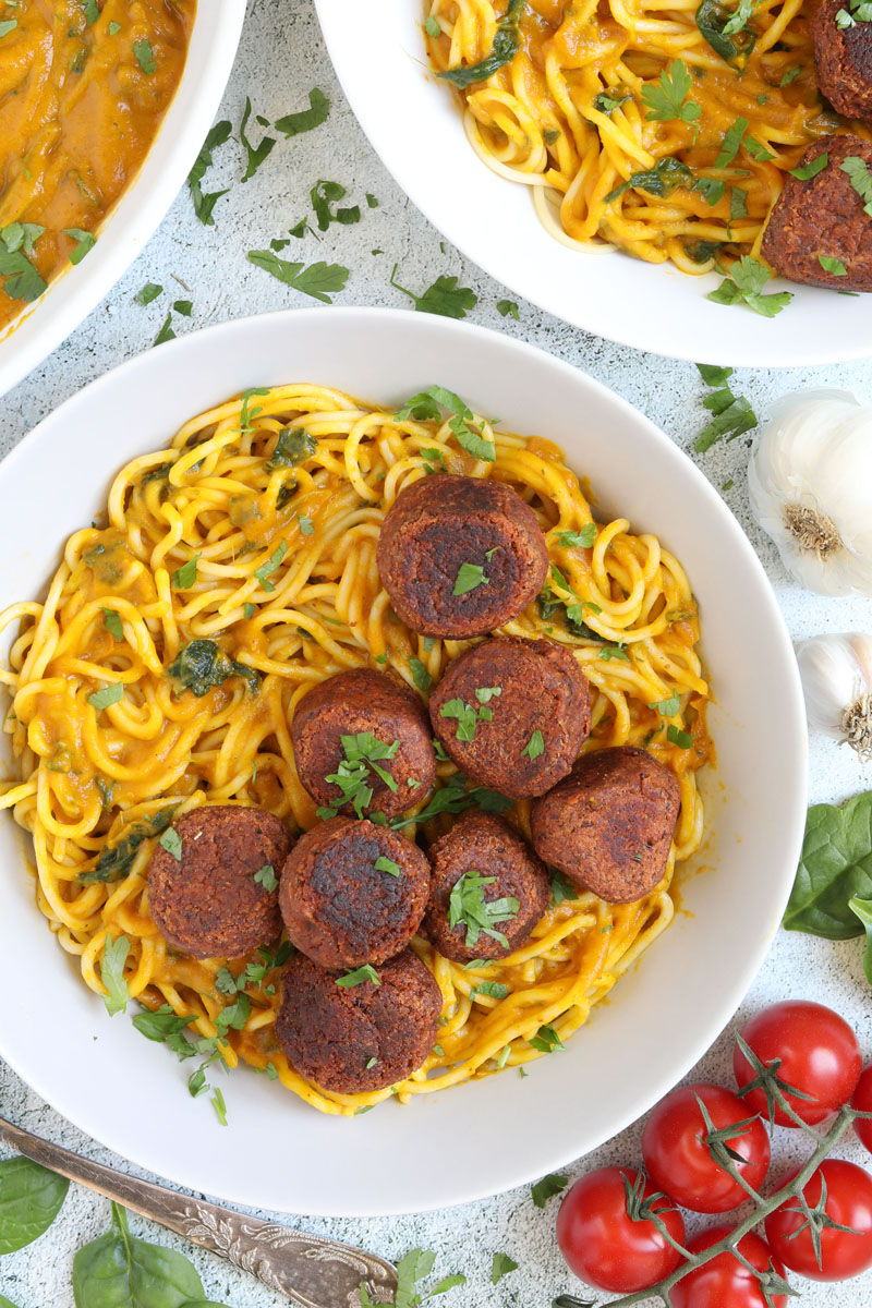 Spaghetti with thick orange sauce served with brown veggie balls in two white bowls. Leftover sauce is in the corner in a small bowl.