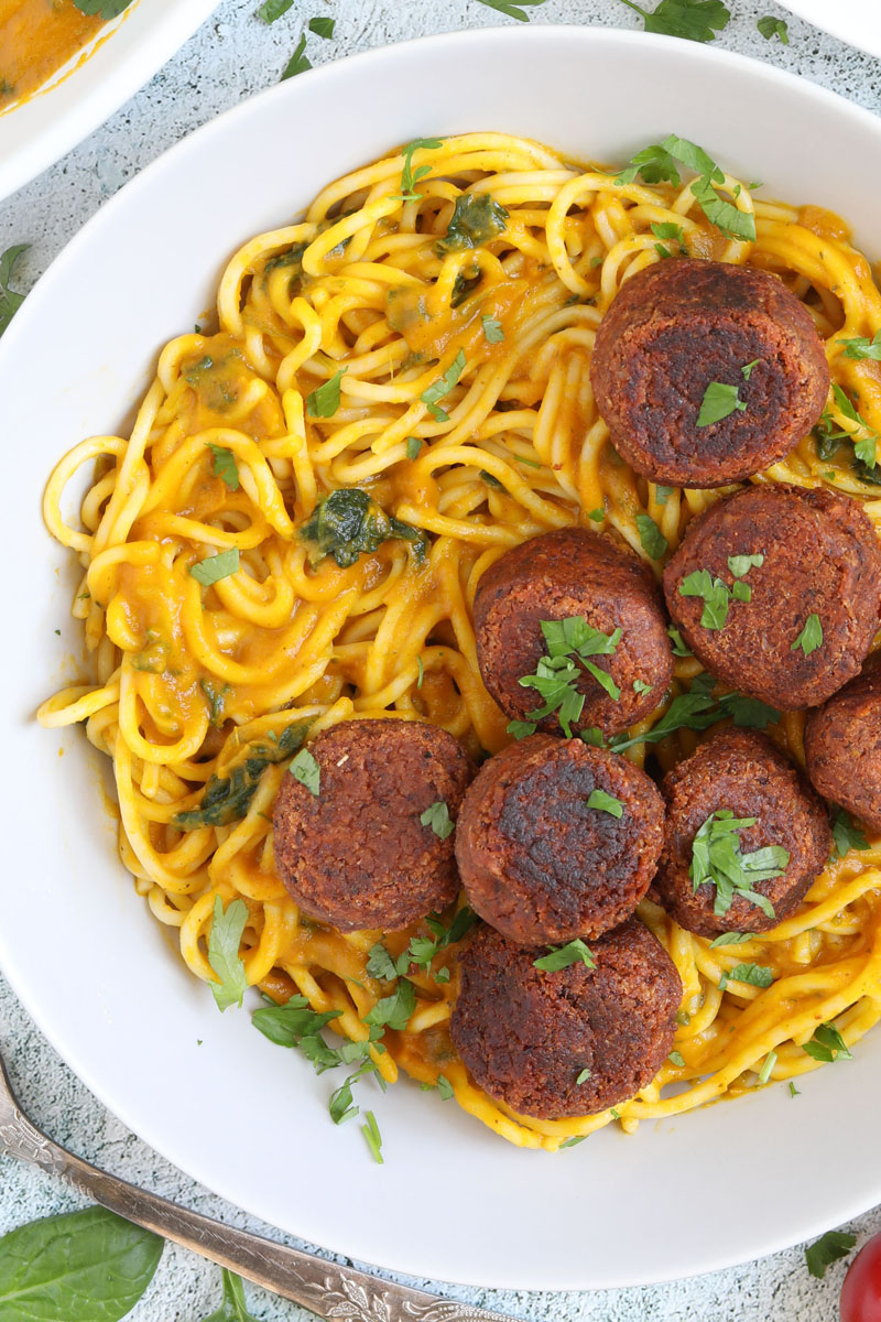Spaghetti with thick orange sauce served with brown veggie balls in a white bowl.