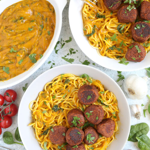 Spaghetti with thick orange sauce served with brown veggie balls in two white bowls. Leftover sauce is in the corner in a small bowl.