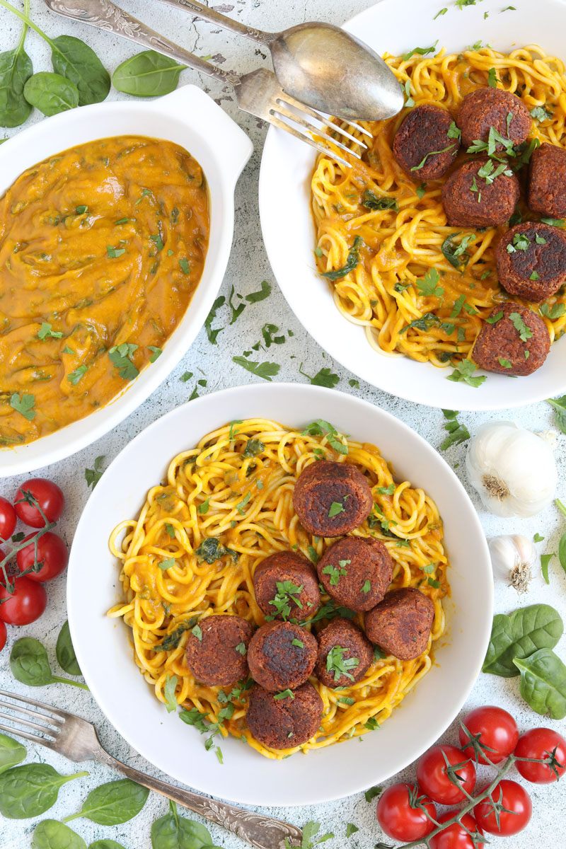 Spaghetti with thick orange sauce served with brown veggie balls in two white bowls. Leftover sauce is in the corner in a small bowl.