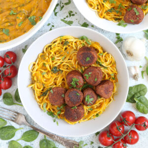 Spaghetti with thick orange sauce served with brown veggie balls in two white bowls. Leftover sauce is in the corner in a small bowl.