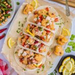 4 small tortillas folded in half on parchment paper filled with cauliflower florets, tomato, and onion pieces drizzled with a light pink sauce. Green beans, and chickpeas are served as a side.