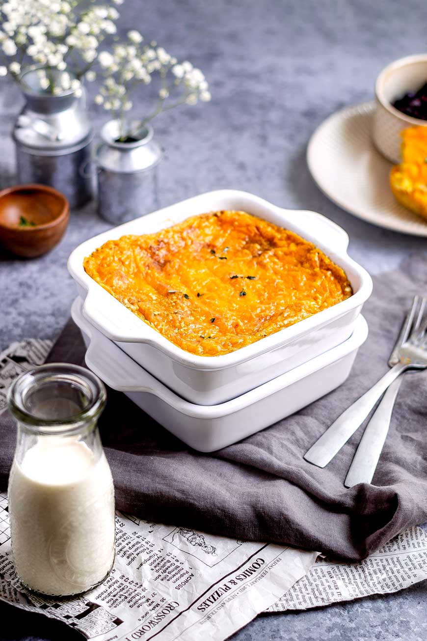 A small white baking pan with cheezy casserole served on a gray tablecloth