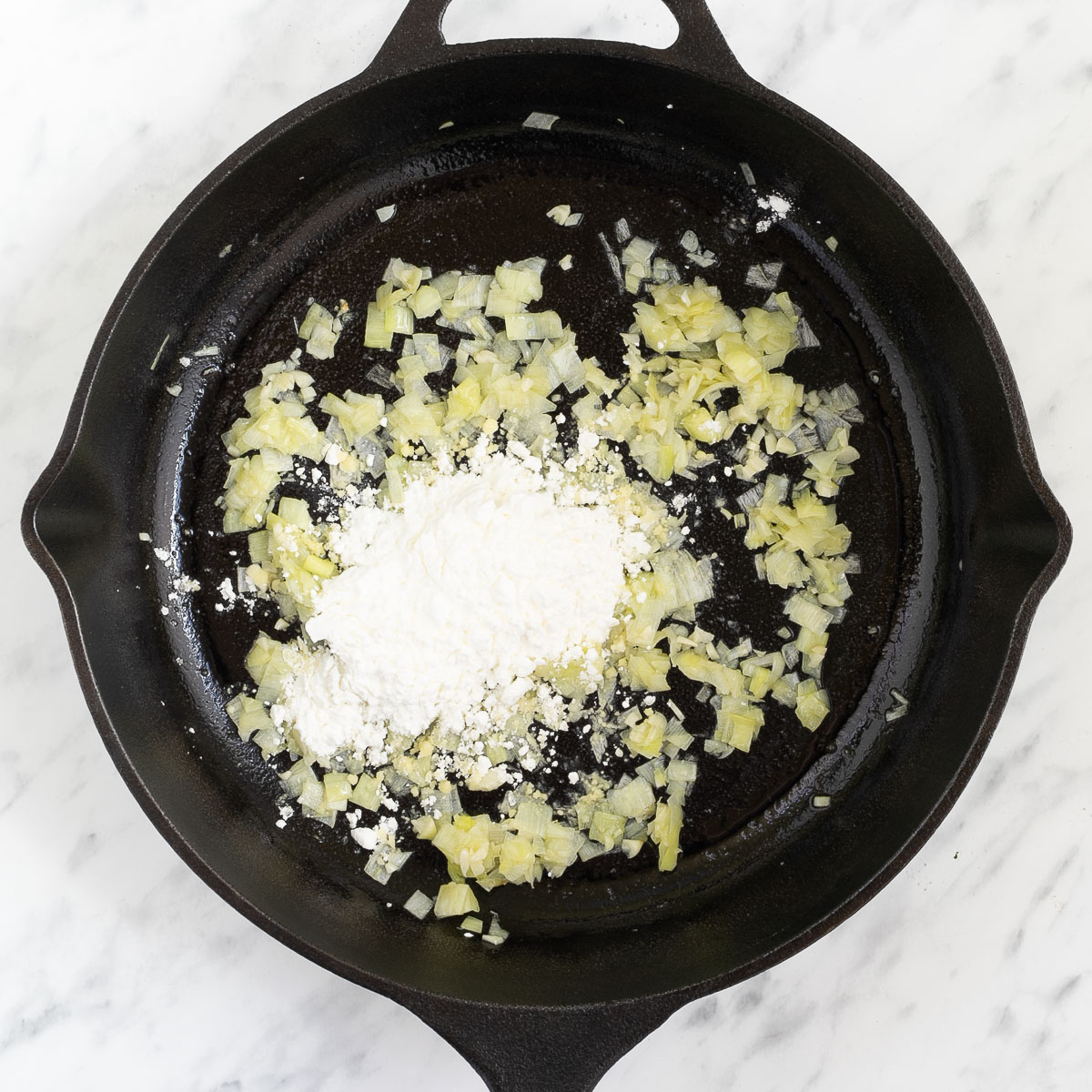Black cast iron skillet with finely chopped onion and garlic.
