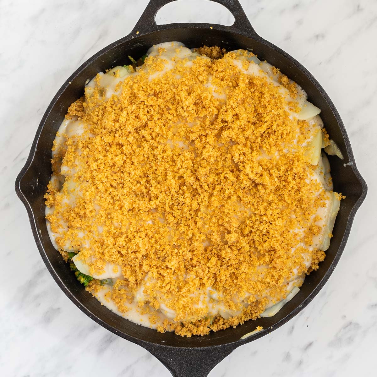 Black cast iron with ingredients in a thick yellow sauce topped with yellow breadcrumbs.