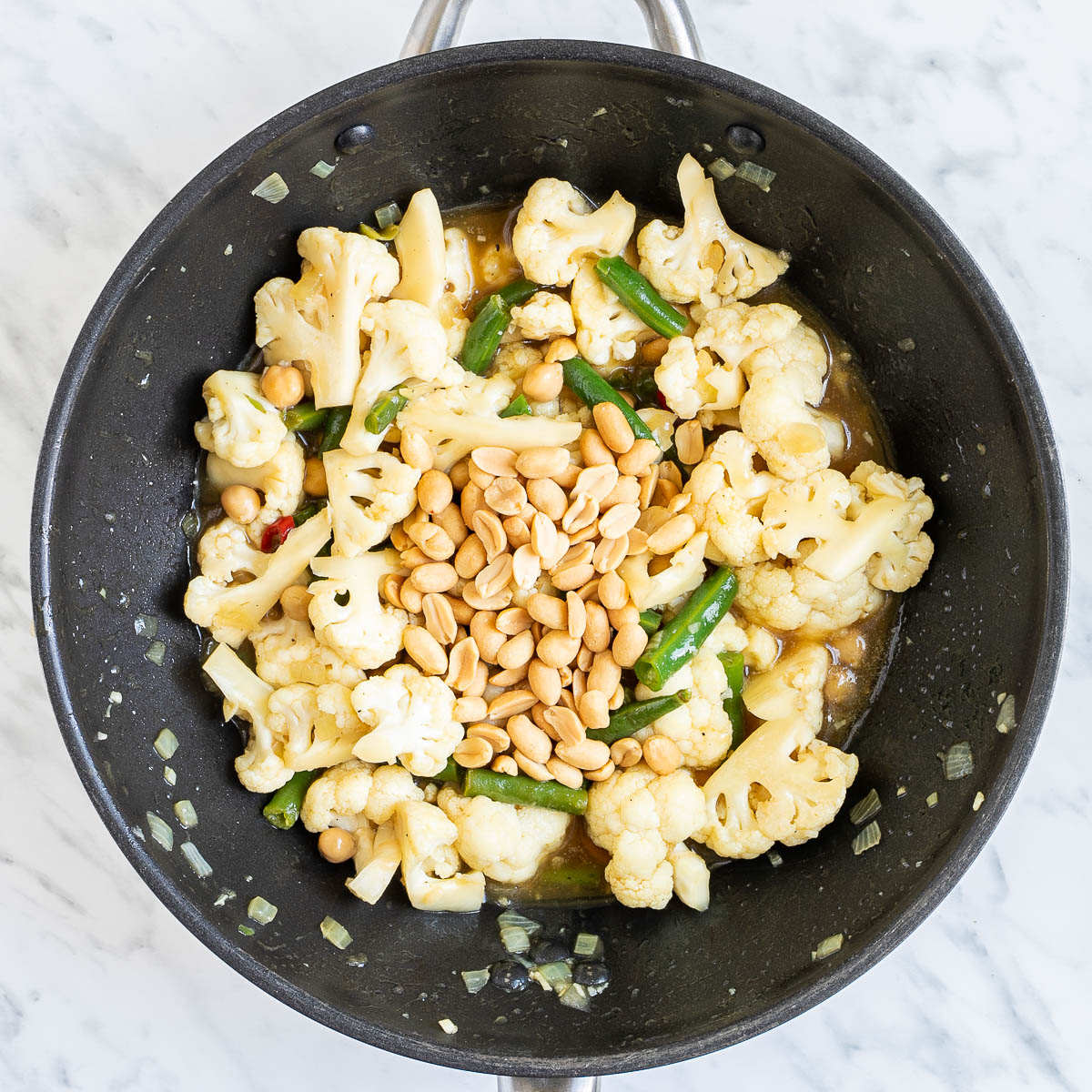 Wok with cauliflower florets, chickpeas, peanuts and green beans in a light brown sauce