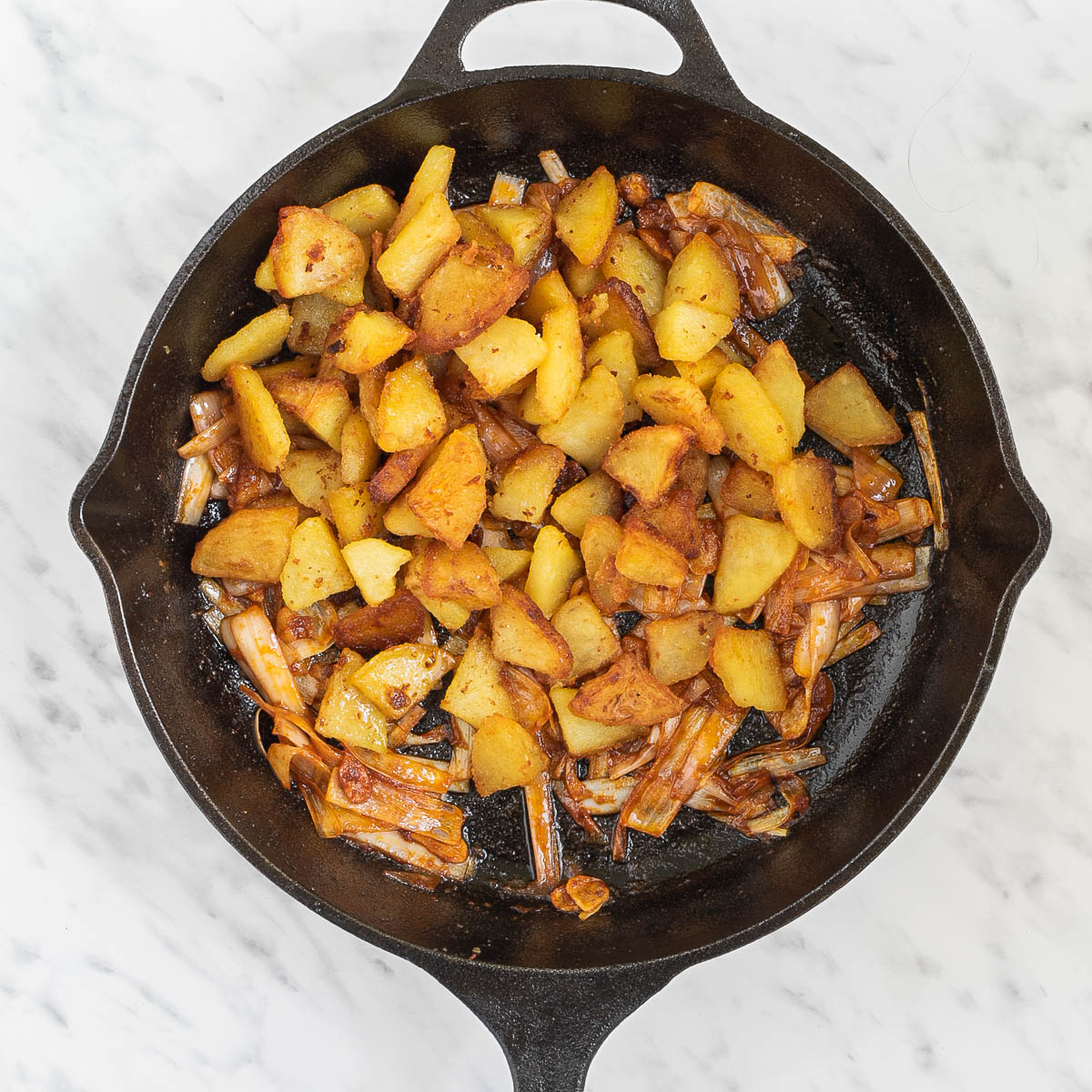 Skillet with potatoes and caramelized onion slices.