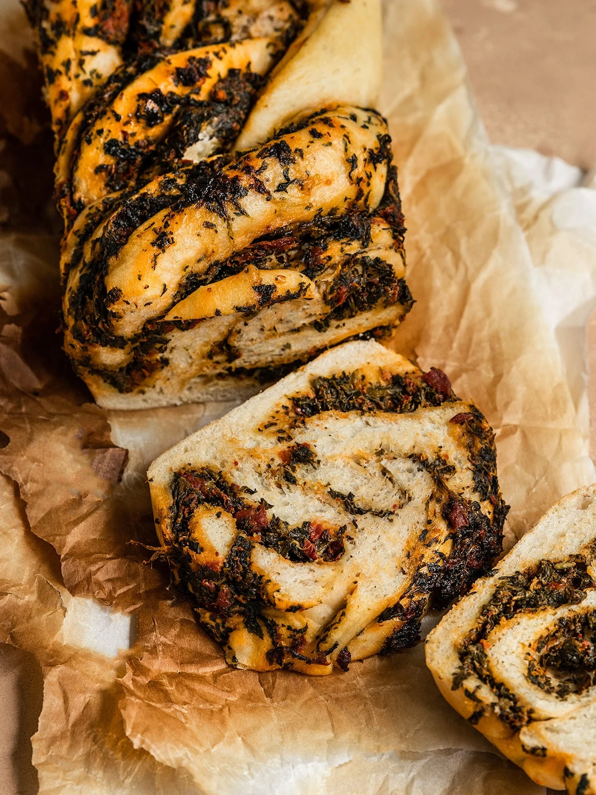 A babka loaf with pesto swirls on a baking paper. 2 slices are cut down and placed to the front.