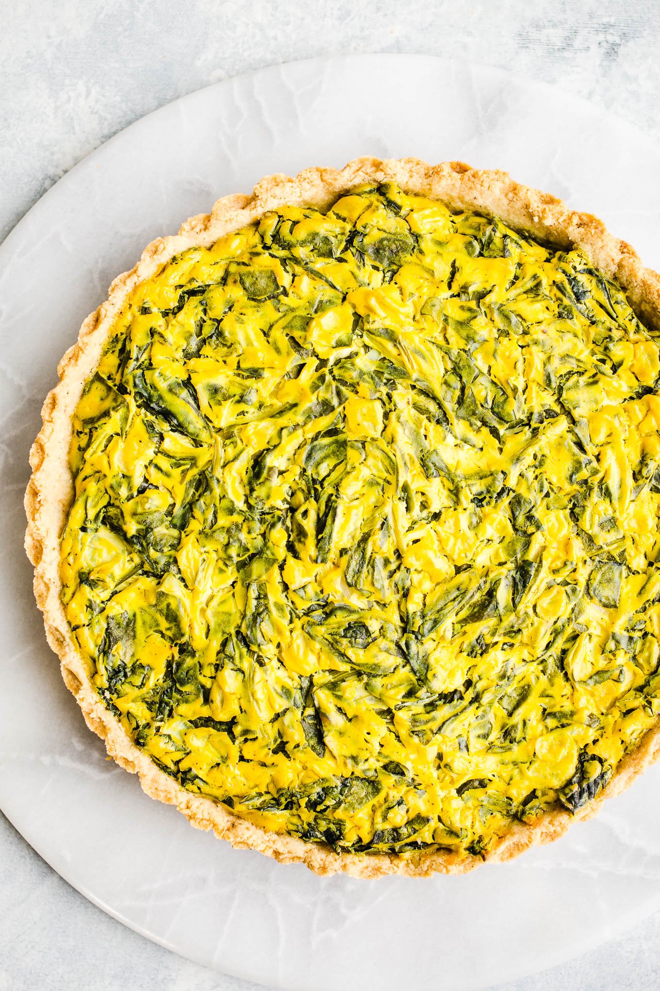 A round large yellow quiche with crust full of wilted spinach leaves.
