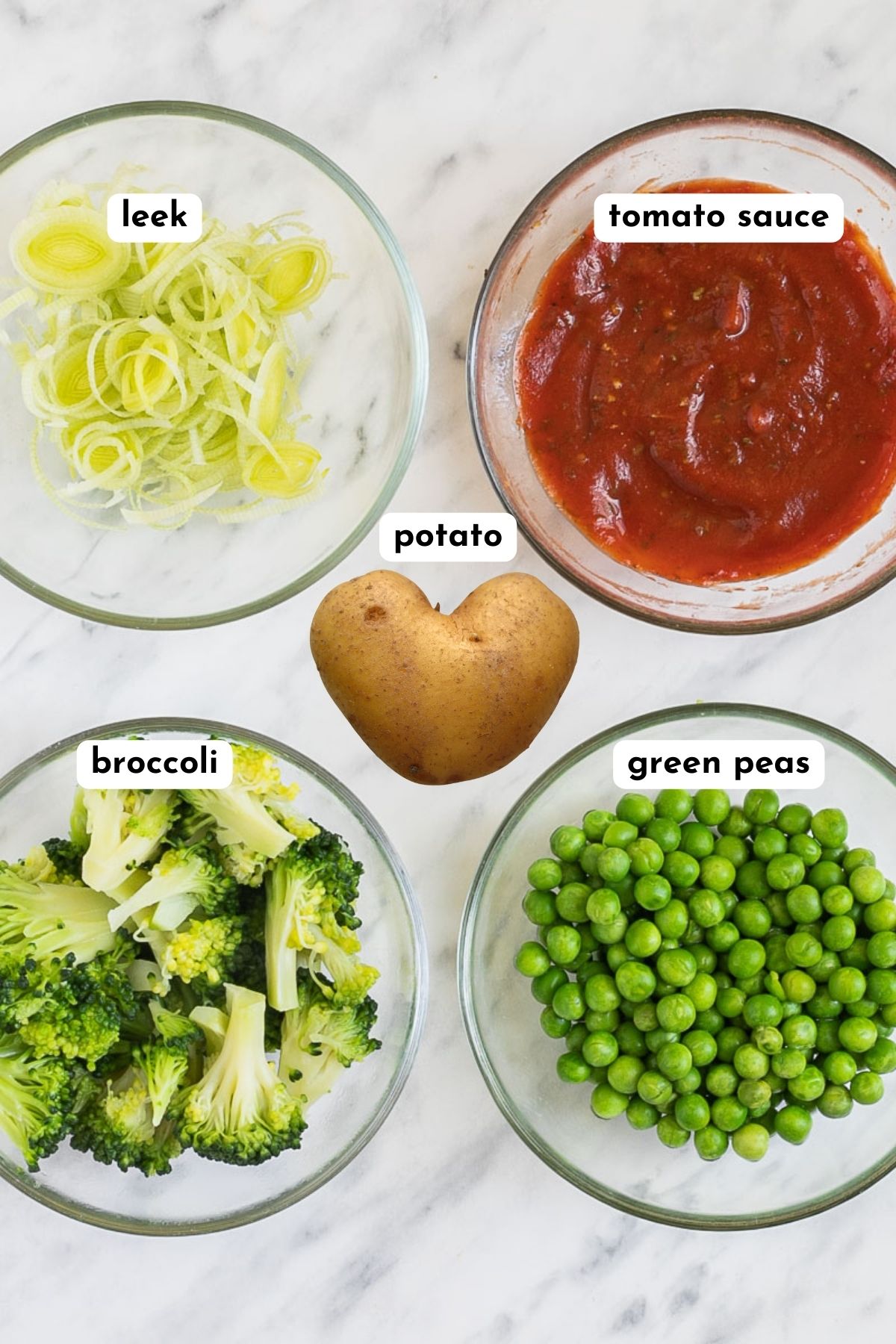 Ingredients of vegan breakfast pizza in small bowls like leek, tomato sauce, broccoli florets, green peas, and potatoes. 