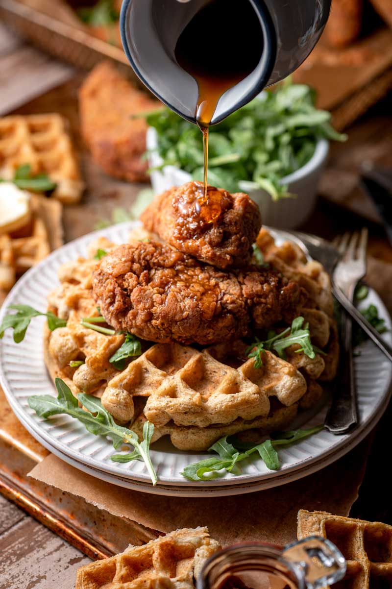 A white plate of large round waffle topped with fried chicken sticks.