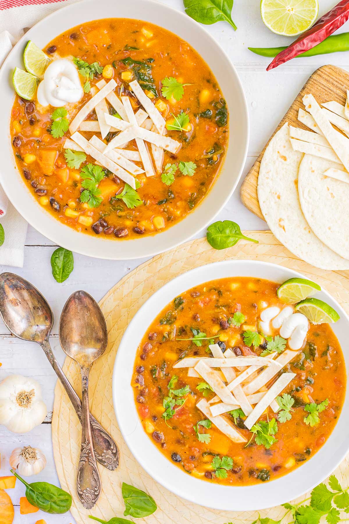 2 white bowls of orange soup loaded with beans, corn, and topped with tortilla strips and freshly chopped cilantro