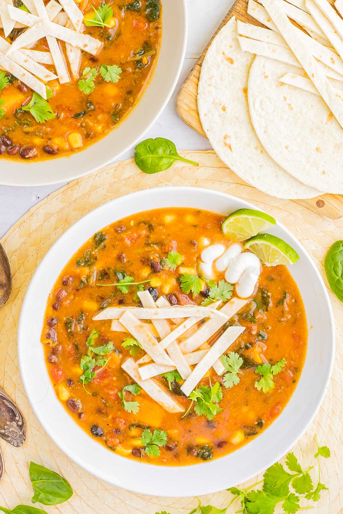 2 white bowls of orange soup loaded with beans, corn, and topped with tortilla strips and freshly chopped cilantro. More tortilla on the side. 