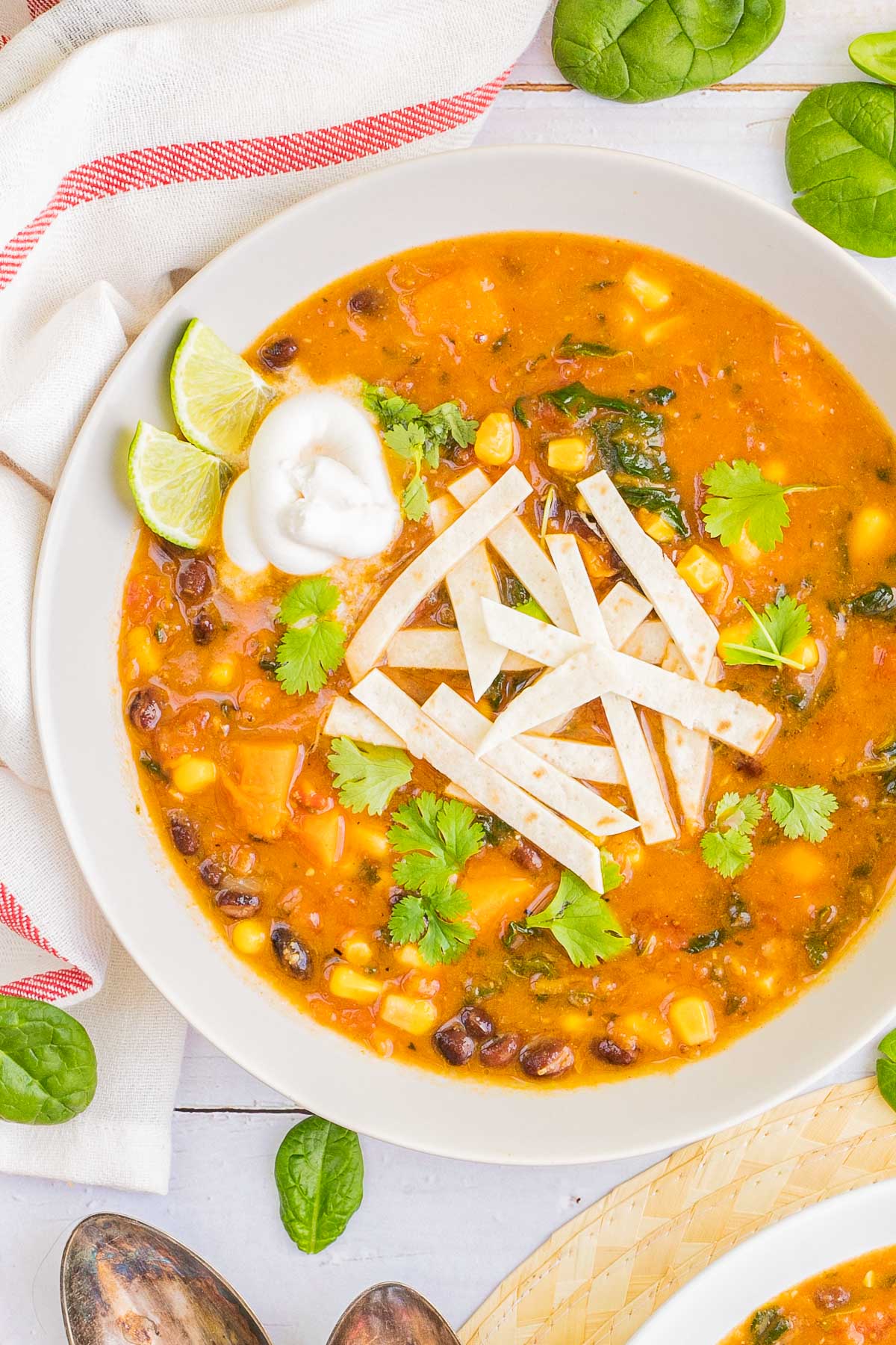 A white bowl of orange soup loaded with beans, corn, and topped with tortilla strips and freshly chopped cilantro