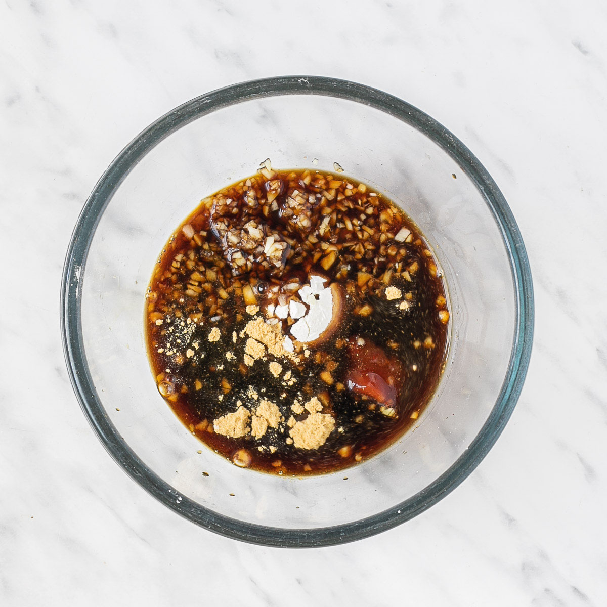 Small glass bowl with dark brown soy sauce and small heaps of different spices.