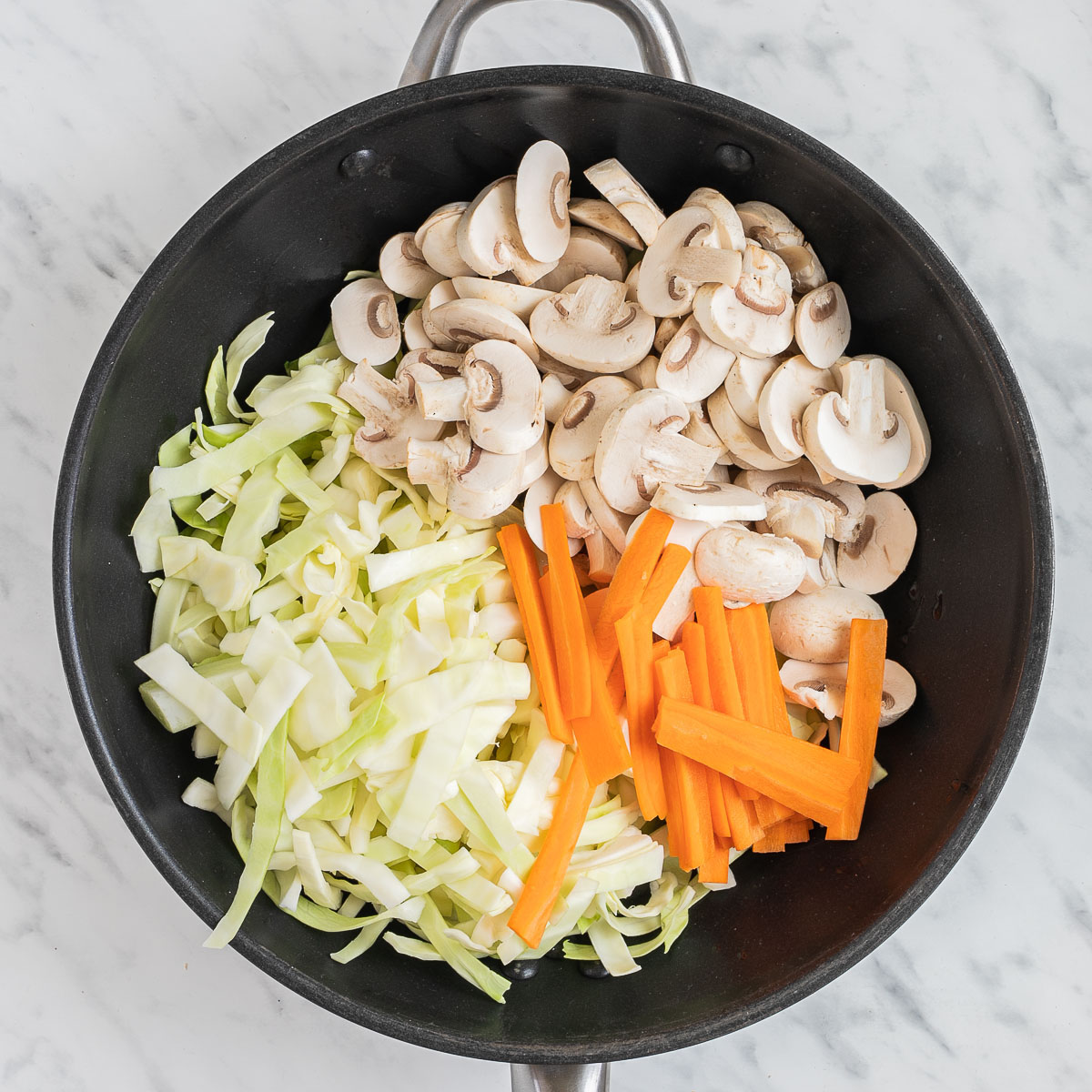 A wok with sliced mushrooms, shredded cabbage and sliced carrots.