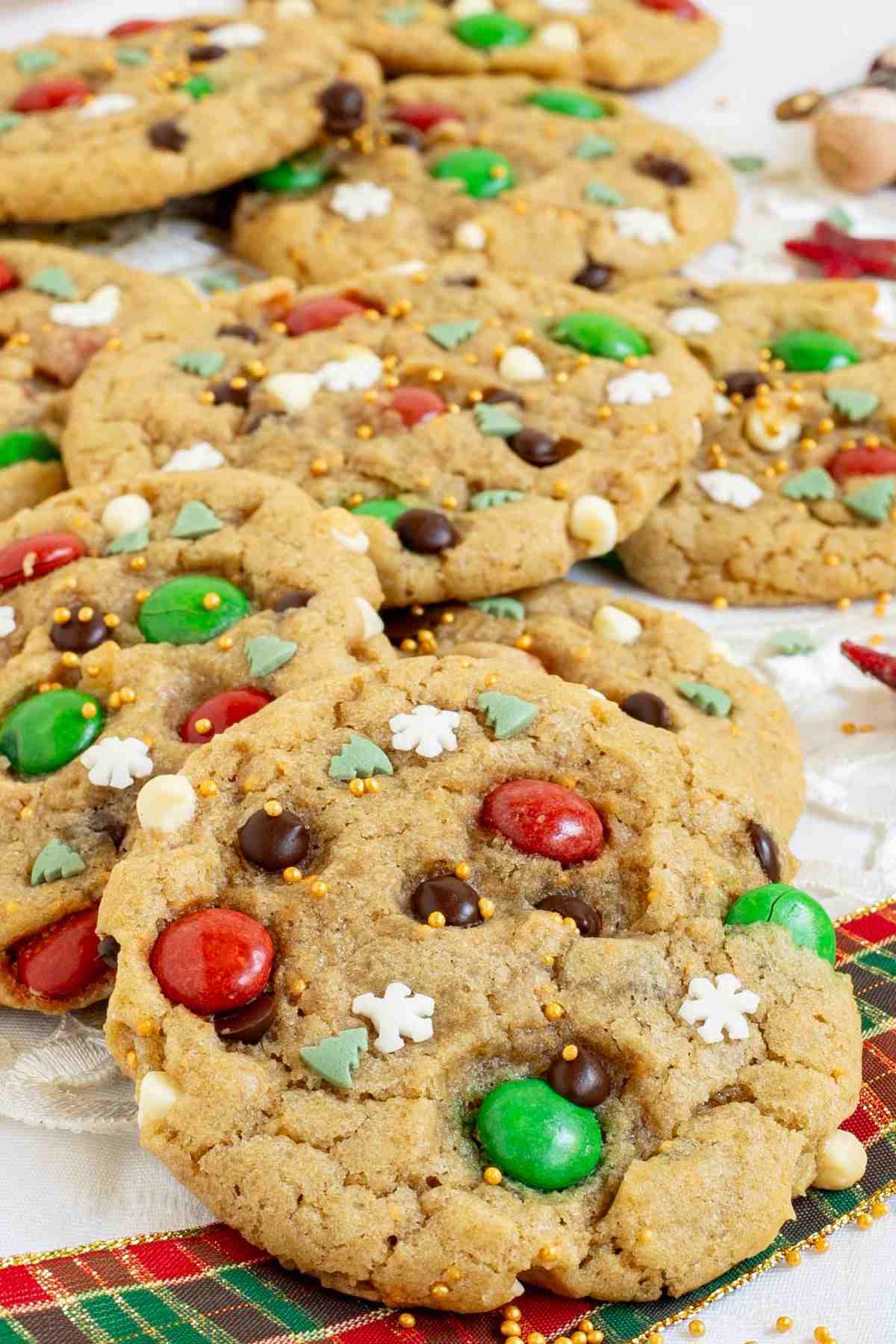 Light brown cookies with red and green m&ms, chocolate chips, tiny white sugar snowflakes, and tiny green pine trees.