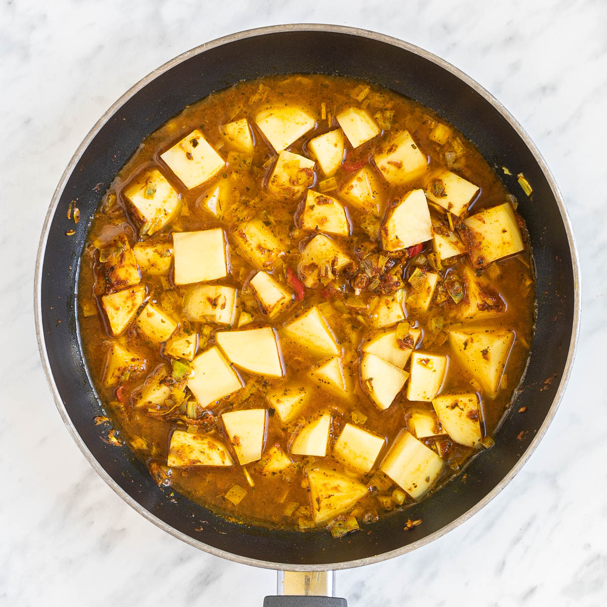 Diced potatoes in an orange thin sauce in a frying pan.