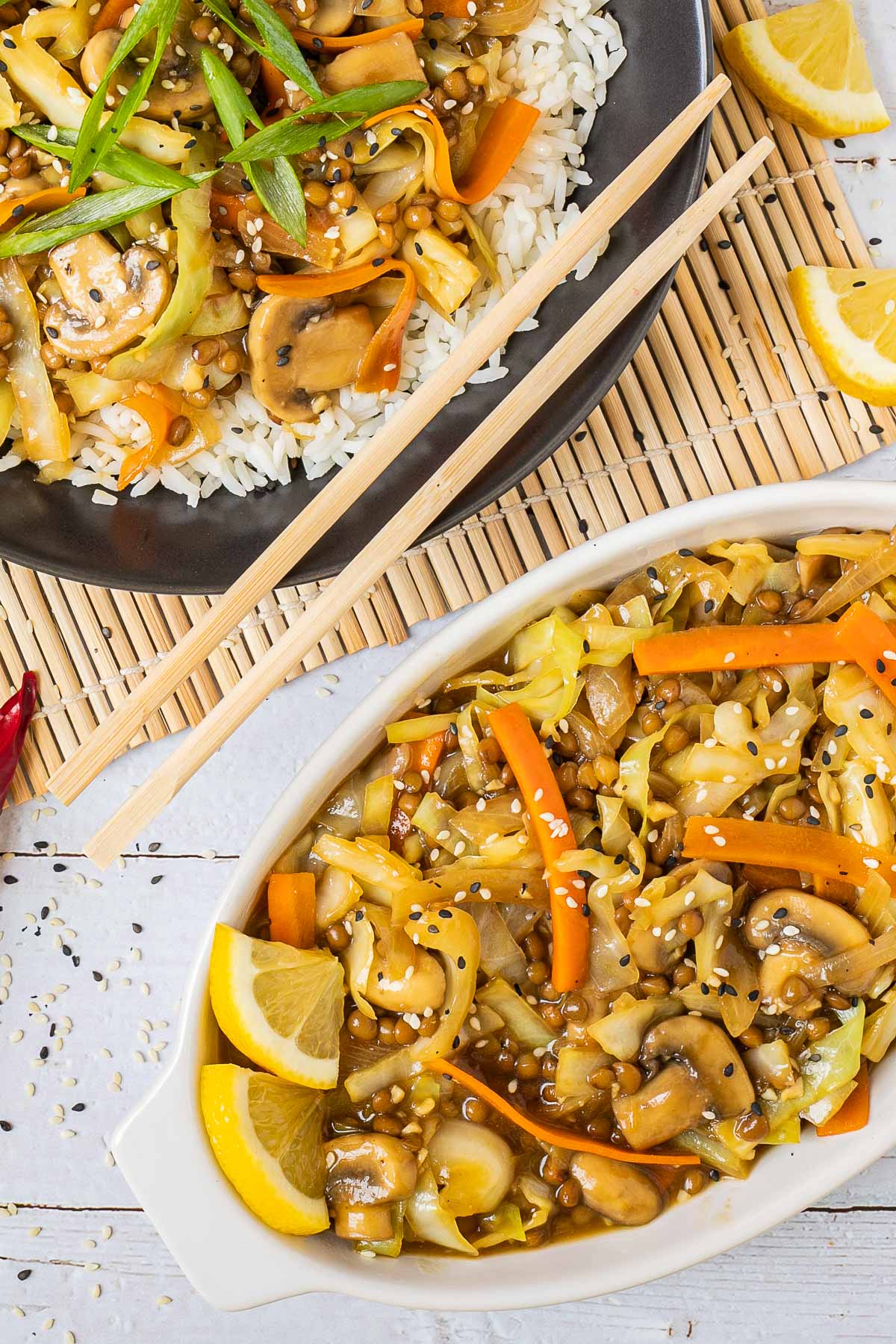 Black plate with white rice topped with stir fired cabbage, mushroom, carrot and lentils. A pair of chopsticks is placed on the side. More stir fried veggies are placed in a separate white bowl.