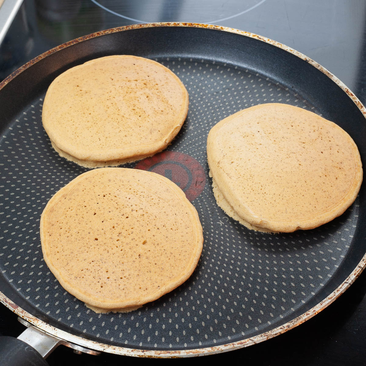 Frying pan with three pancakes that were just turned over.