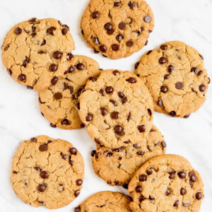 Lots of chocolate chip cookies on a white wooden surface.