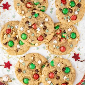 Light brown cookies with red and green m&ms, chocolate chips, tiny white sugar snowflakes, and tiny green pine trees.