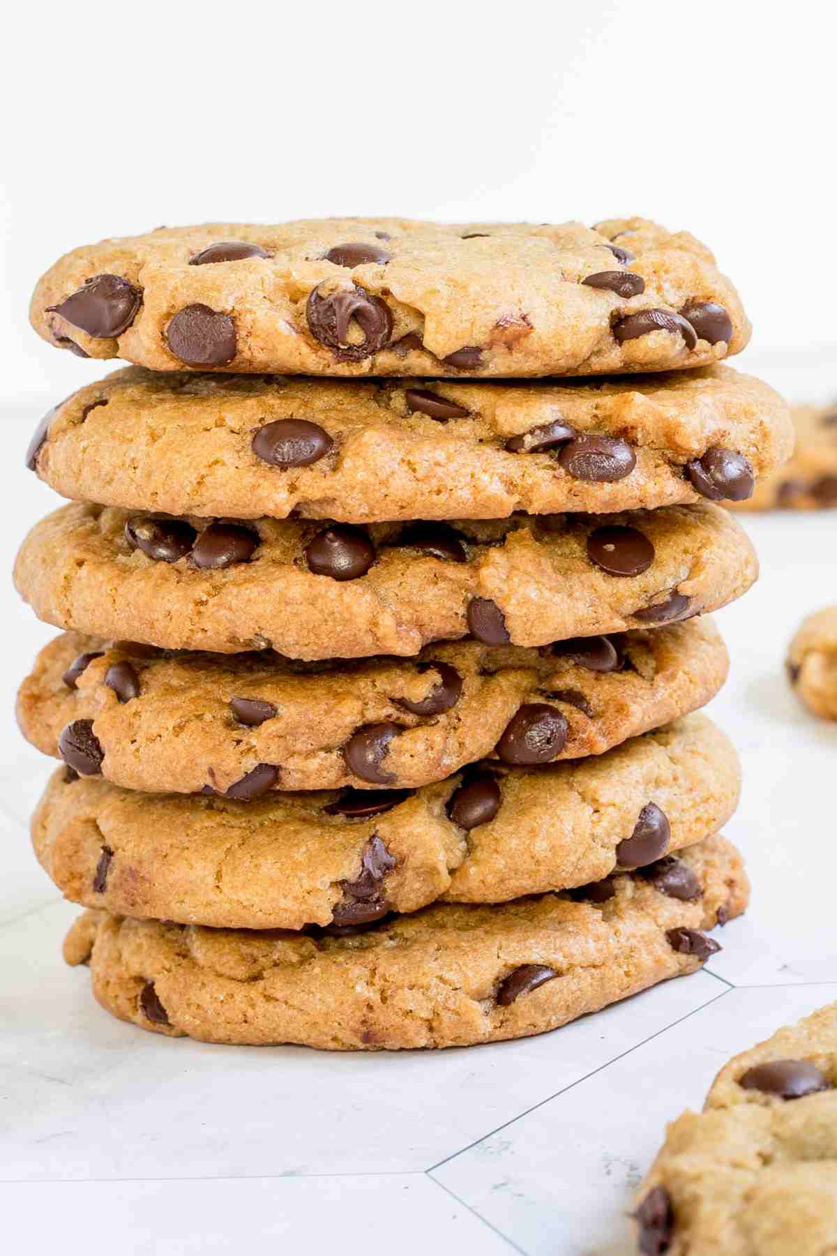 A stack of chocolate chip cookies on a white wooden surface.