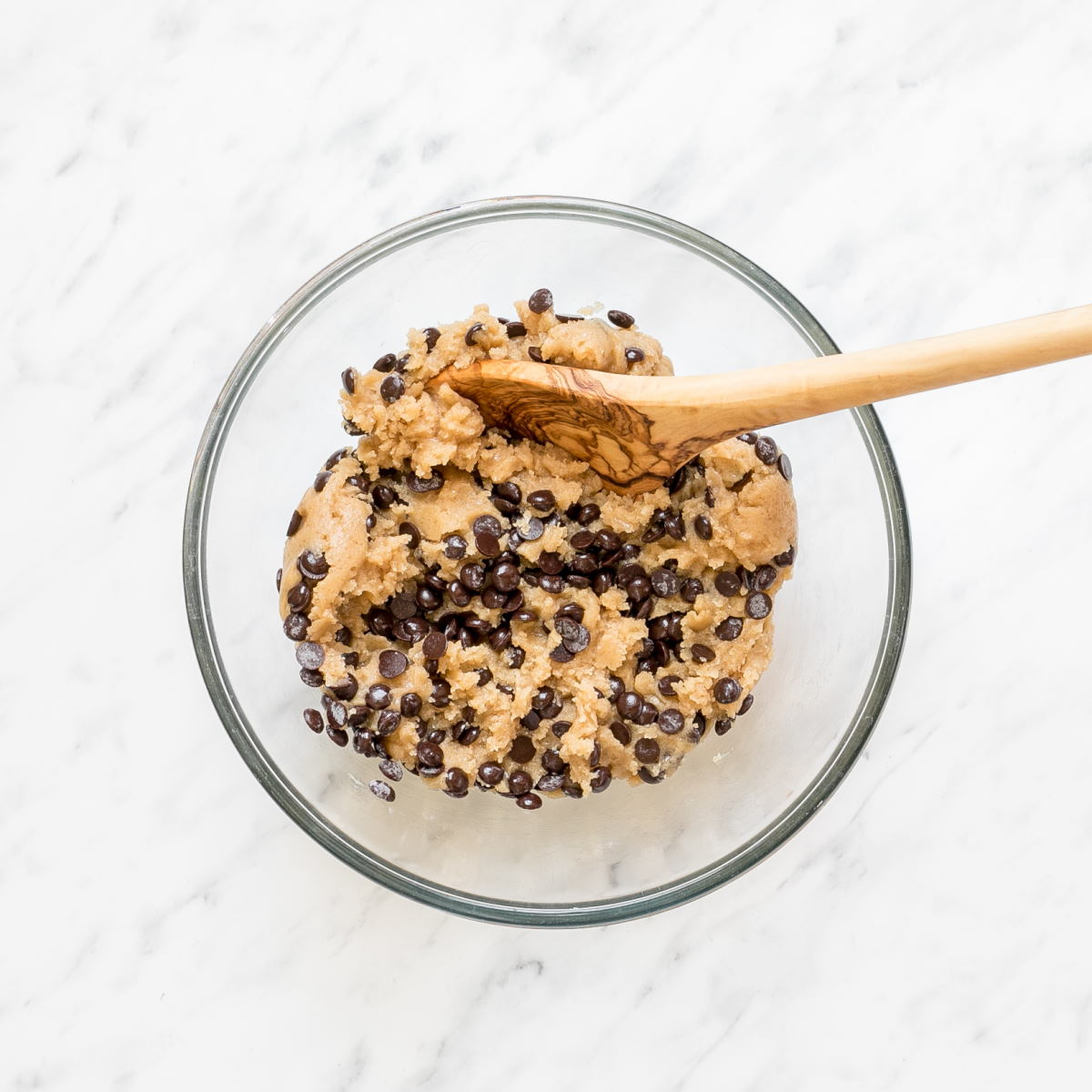 A glass bowl with light brown cookie batter with lots of chocolate chips.
