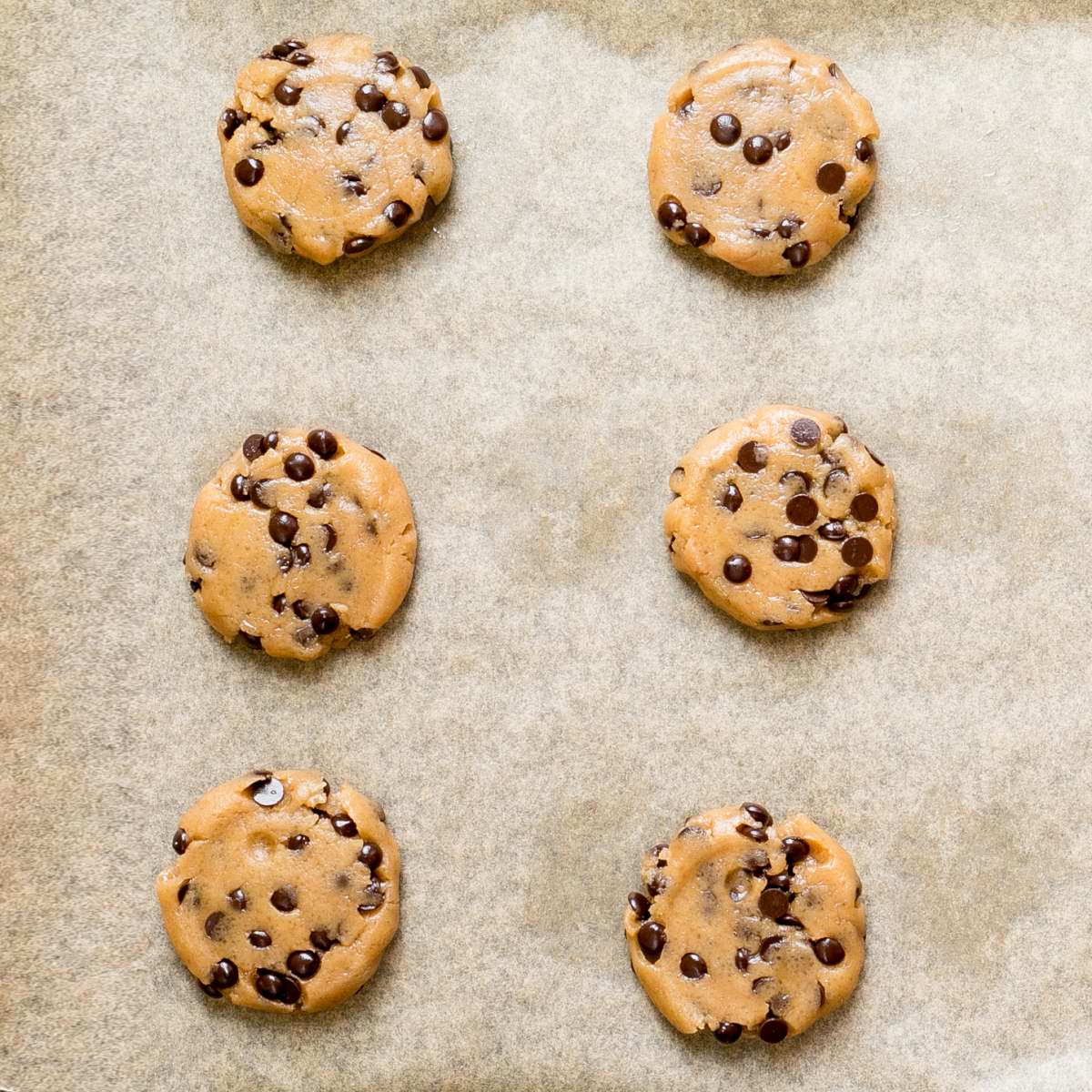 Unbaked round cookie batters with chocolate chips on a parchment paper neatly placed away from each other.