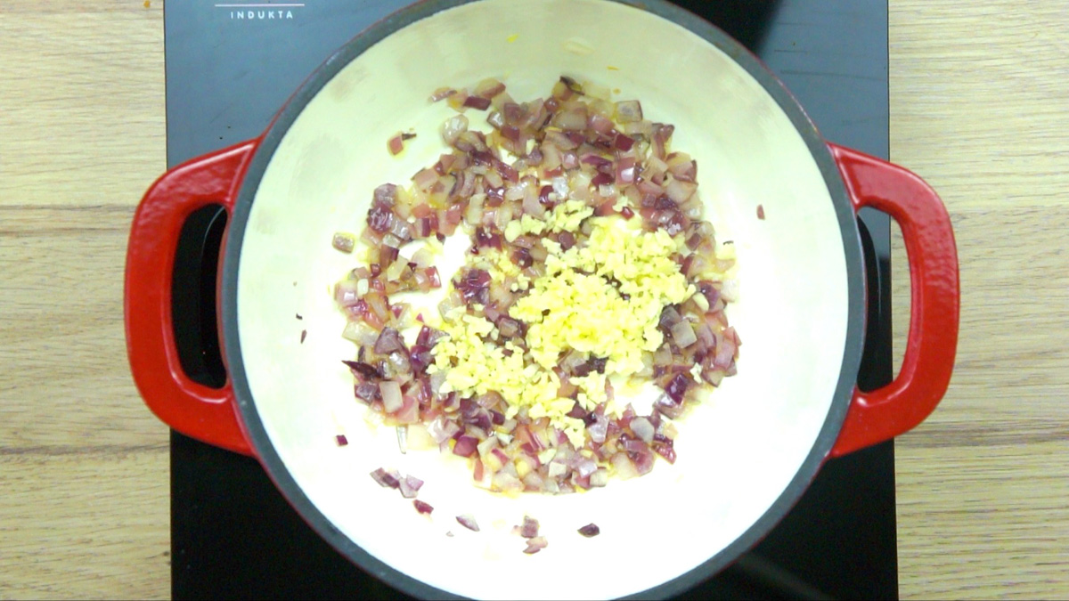 Red-white enameled Dutch oven with minced purple onion and heaps of minced garlic