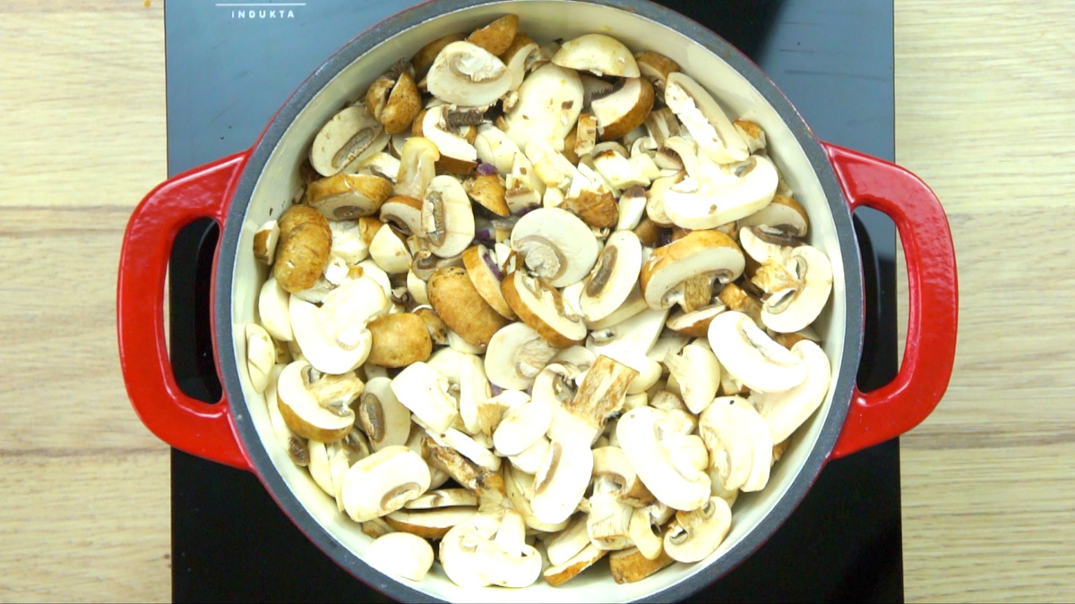 Red-white enameled Dutch oven with full of sliced button mushrooms.