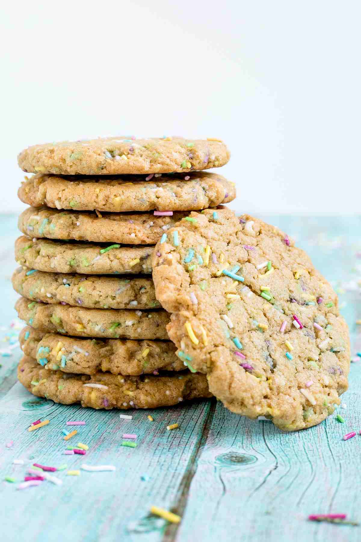 A stack of light brown cookies with rainbow sprinkles on a blue wooden surface.