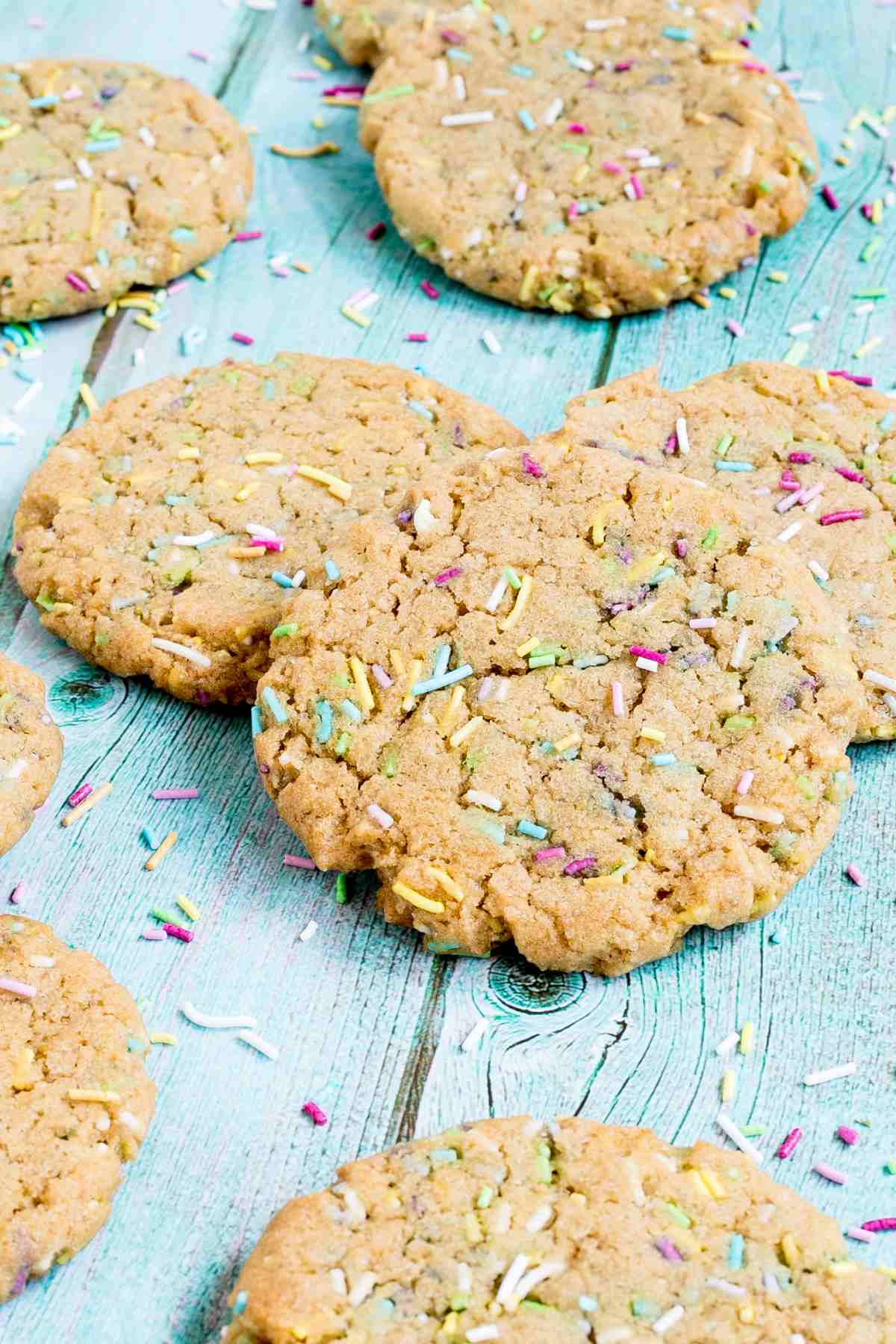 Light brown cookies with rainbow sprinkles on a blue wooden surface.