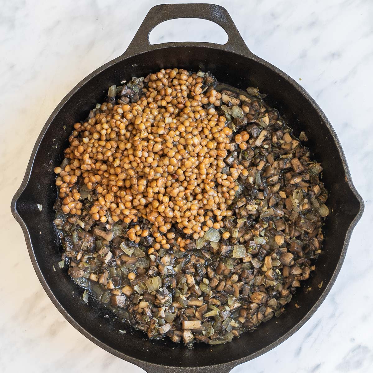 Cast iron skillet with sauteed chopped mushrooms and a heap of brown lentils.