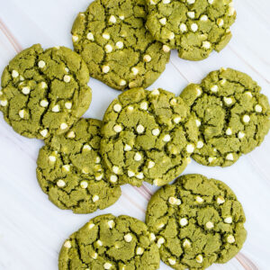 Lots of vibrant green cookies with white chocolate chips on a marble surface.