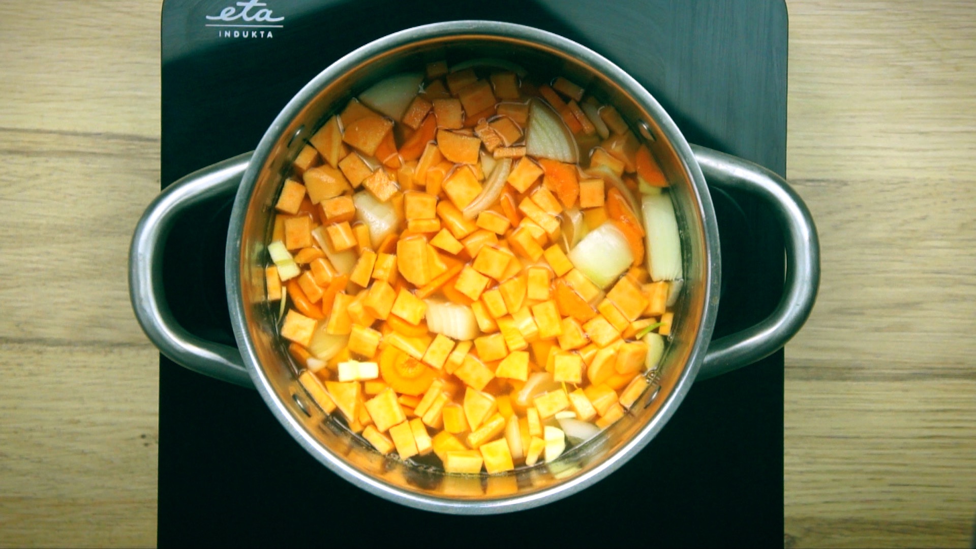 Stockpot with diced carrots, potatoes, orange sweet potatoes, onions and garlic in veggie broth.