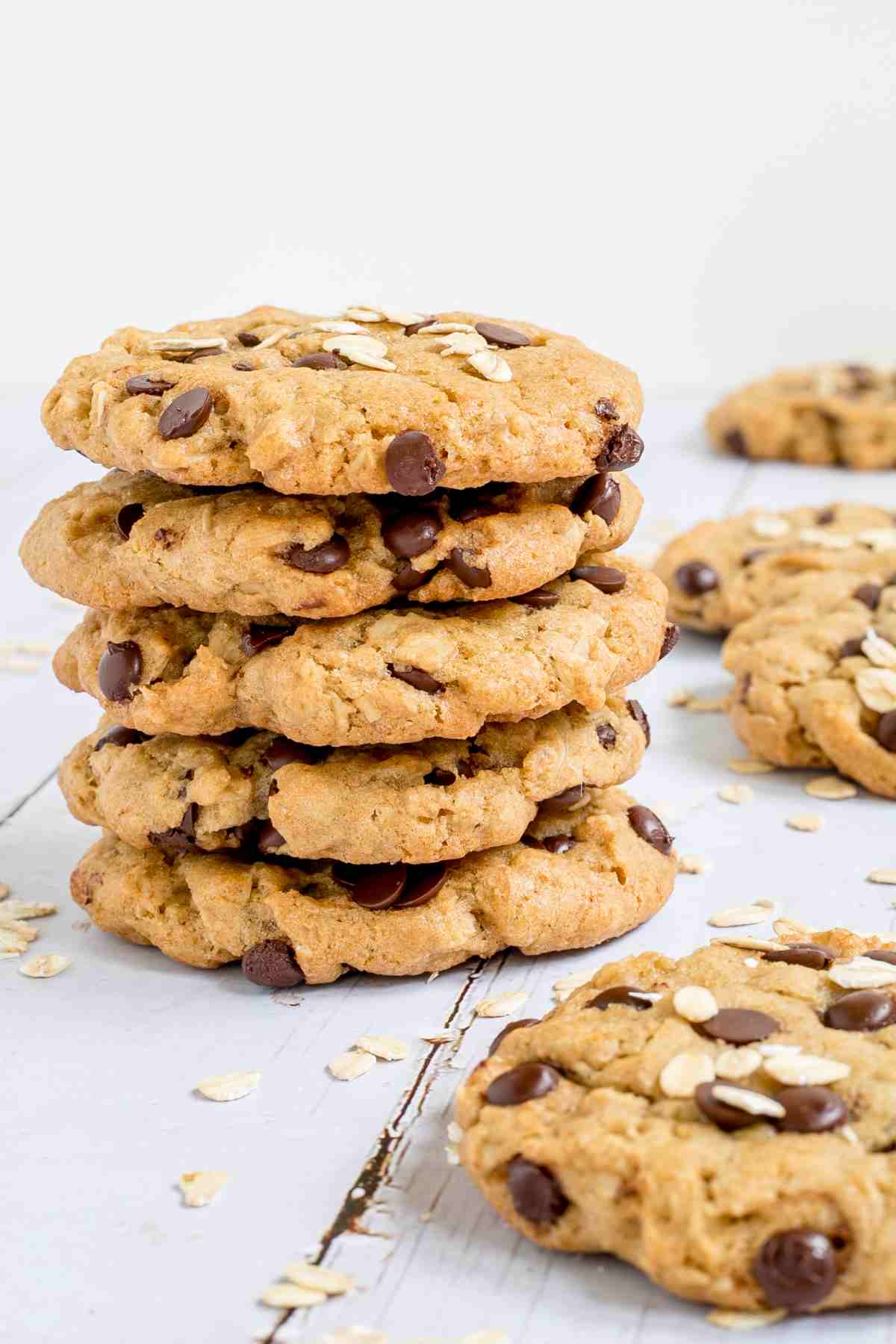 A stack of cookies with oats and chocolate chips on a wooden surface. More oats are sprinkled around them.