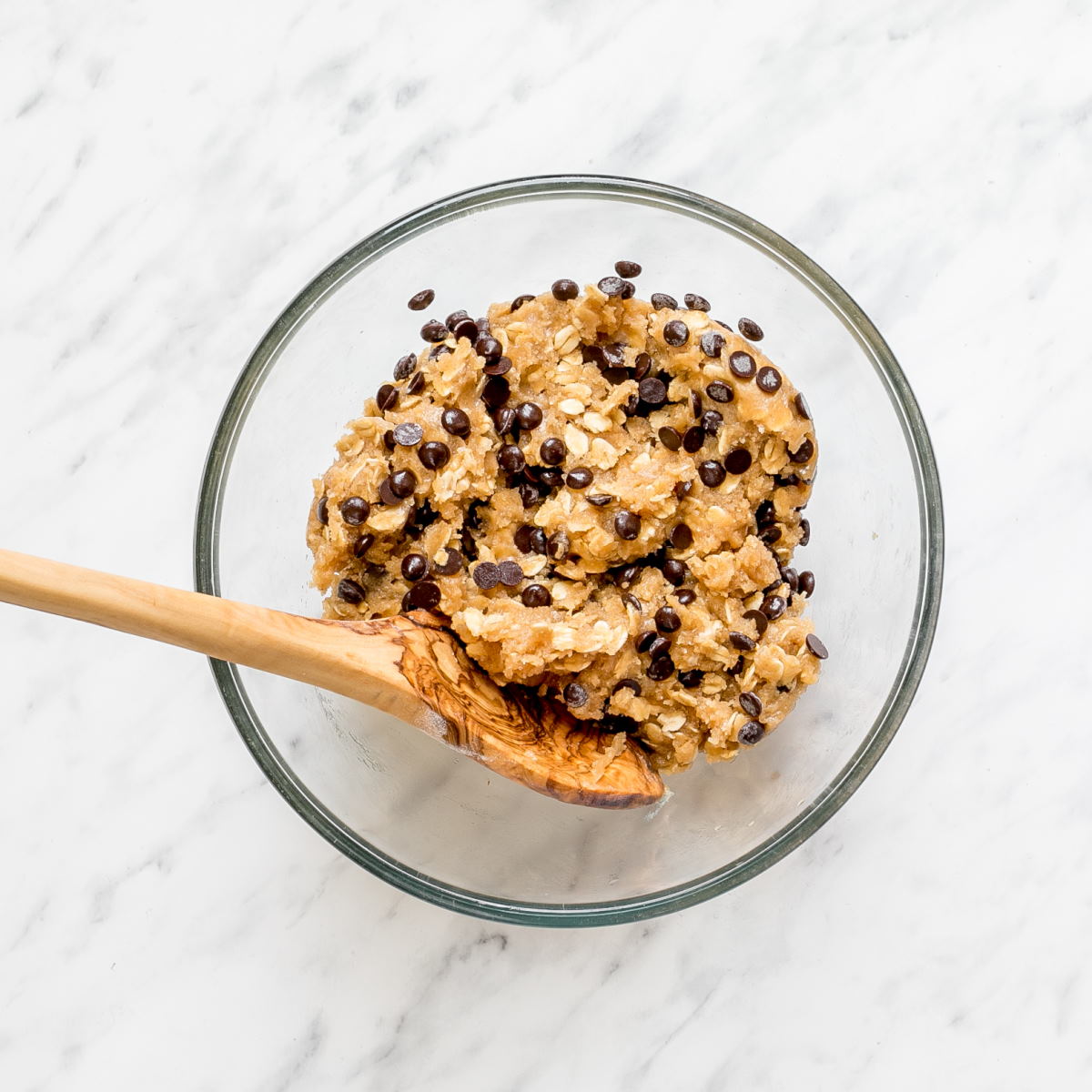 A glass bowl with light brown cookie down with oats and chocolate chips.