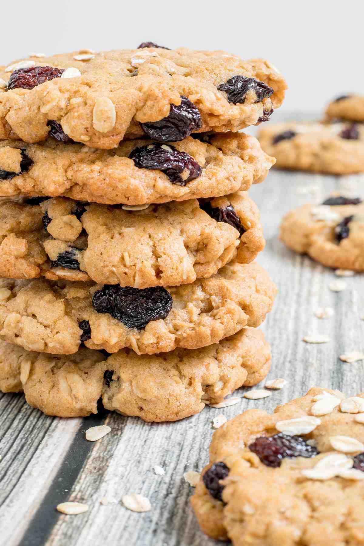 A stack of cookies with oats and raisins on a wooden surface. More oats are sprinkled around them.