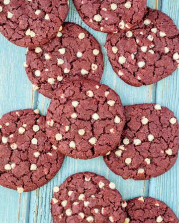 Lot of red velvet cookies with white chocolate chips on a light blue wooden surface.