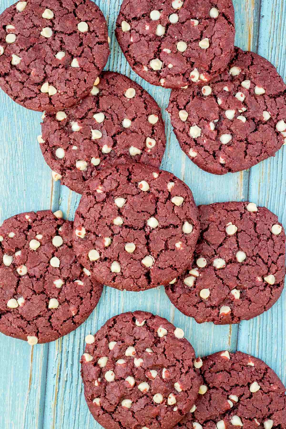 Lot of red velvet cookies with white chocolate chips on a light blue wooden surface. 