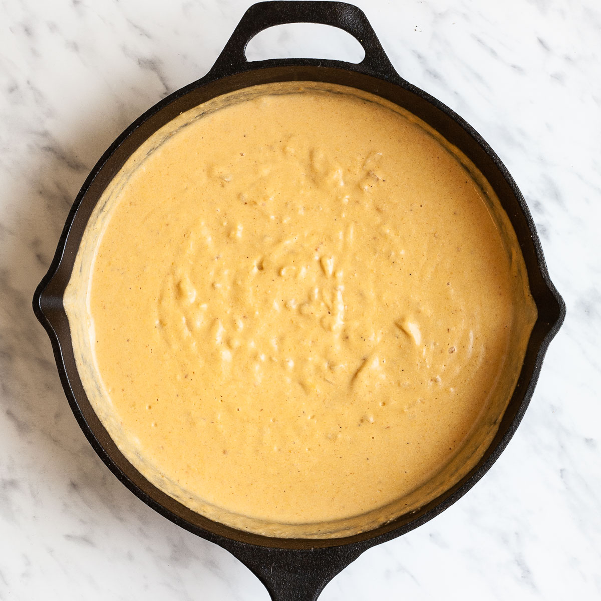 A black cast iron skillet from above full of light brown orange creamy sauce