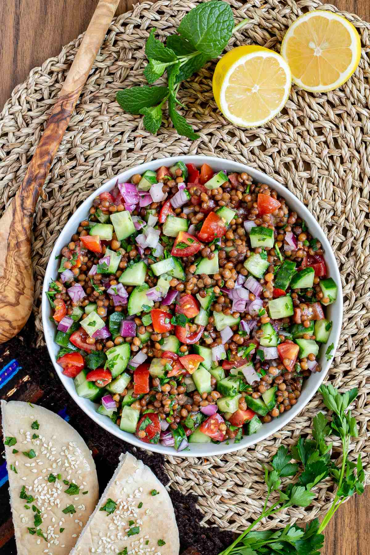 Large white bowl with a chopped mixed salad of brown lentils, cucumber, tomatoes, and red onion.
