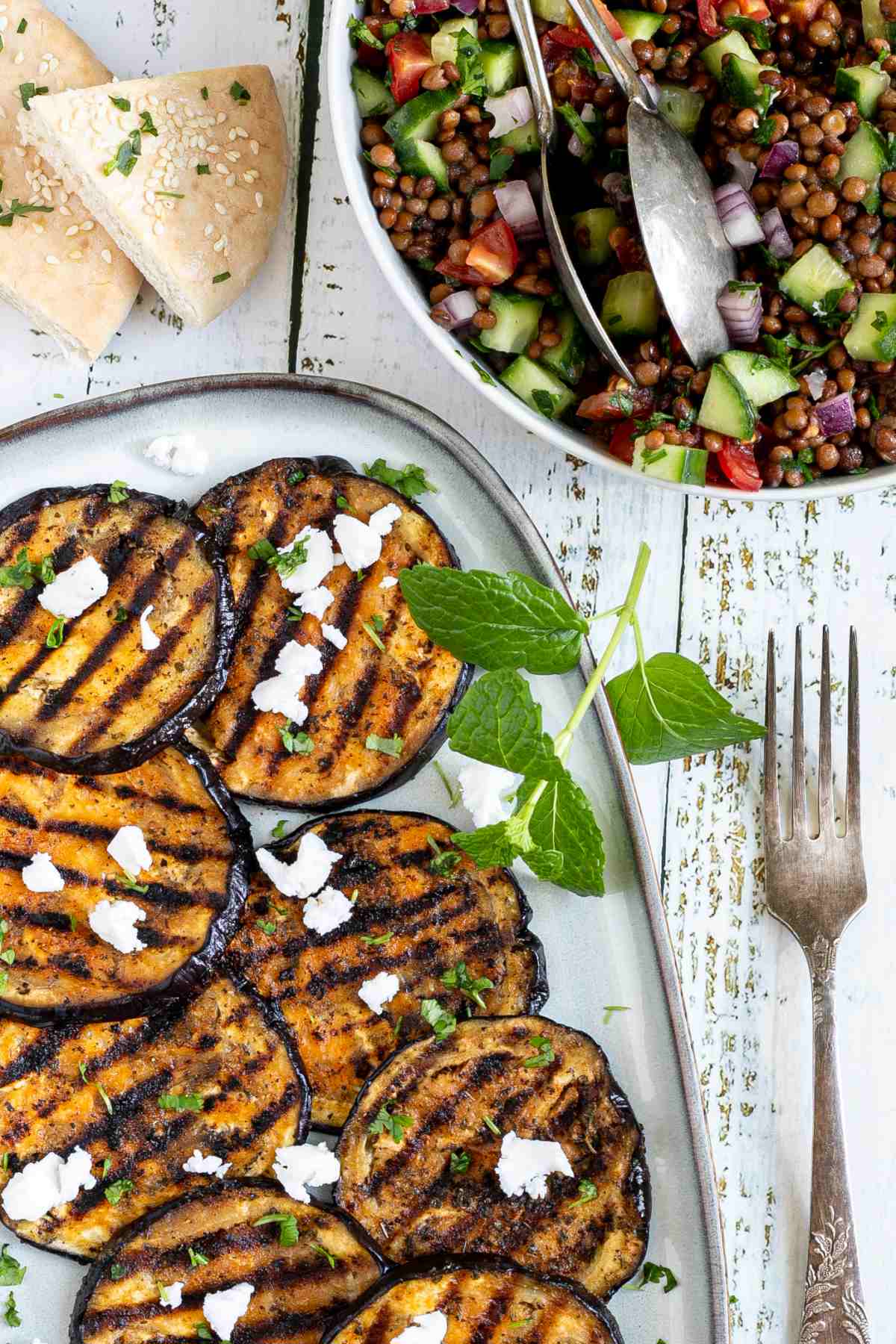 Large grilled slices of eggplant sprinkled with fresh herbs and crumbled cheese served on a light blue plate.