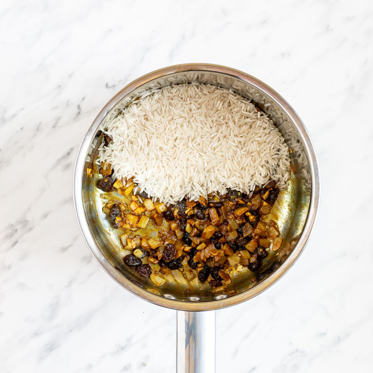 Pan with yellow colored minced onion and raisins and a heap of rice.